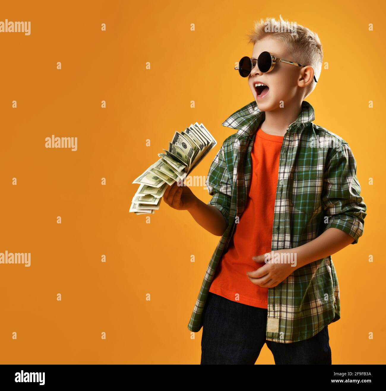 Blond smiling boy child in checkered shirt and sunglasses standing holding heap of money cash dollars in hands having fun Stock Photo