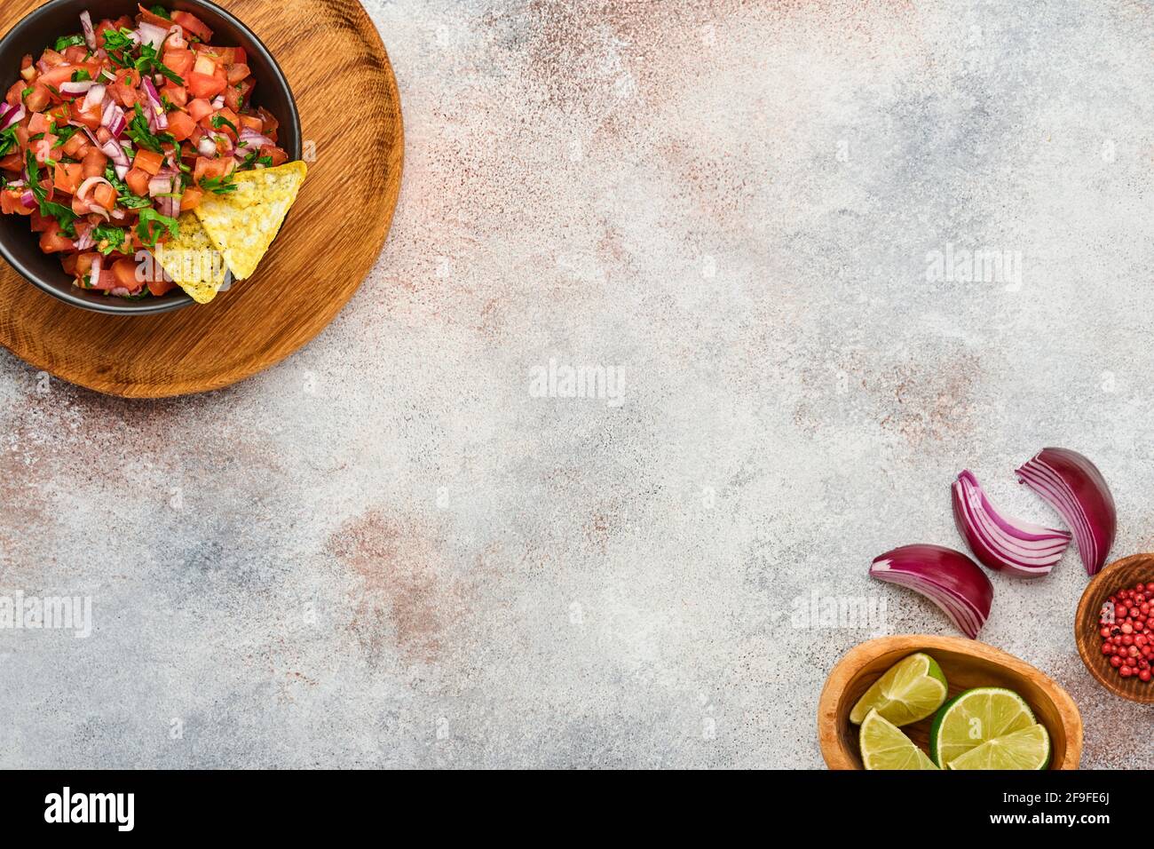 Traditional Mexican tomato sauce salsa with nachos and ingredients tomatoes, chile, garlic, onion on light slate stone background. Concept of Latin Am Stock Photo