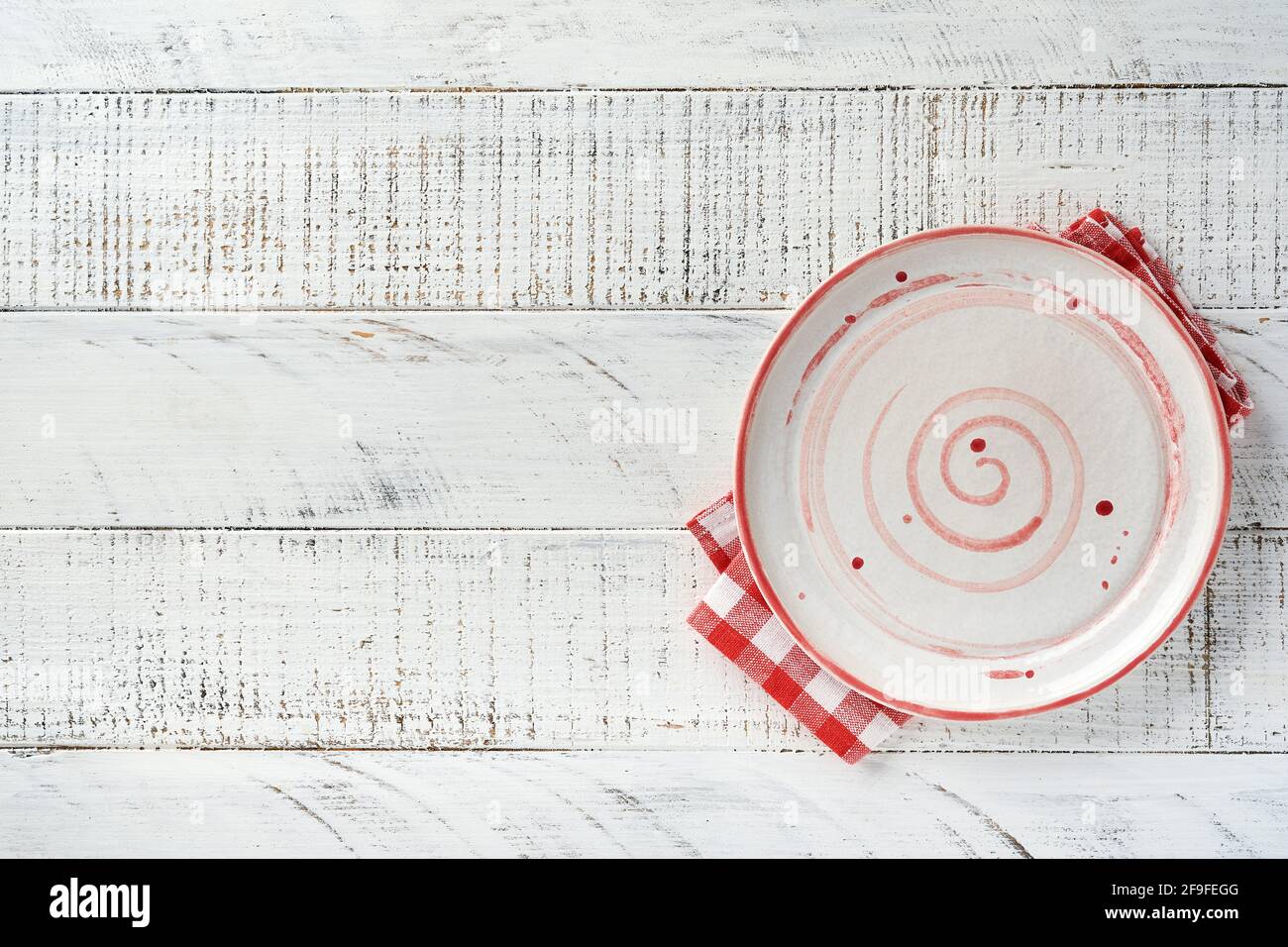 Empty white plate and red towel over old white wooden table background for your recipe or menu. Top view. Mock up. Stock Photo