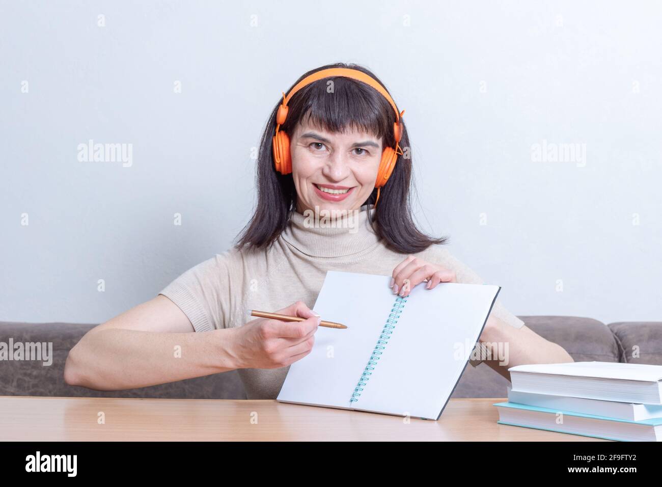 Smiling woman teacher in headphones explains the lesson by showing on a blank exercise book. Back to school concept. Online learning concept Stock Photo