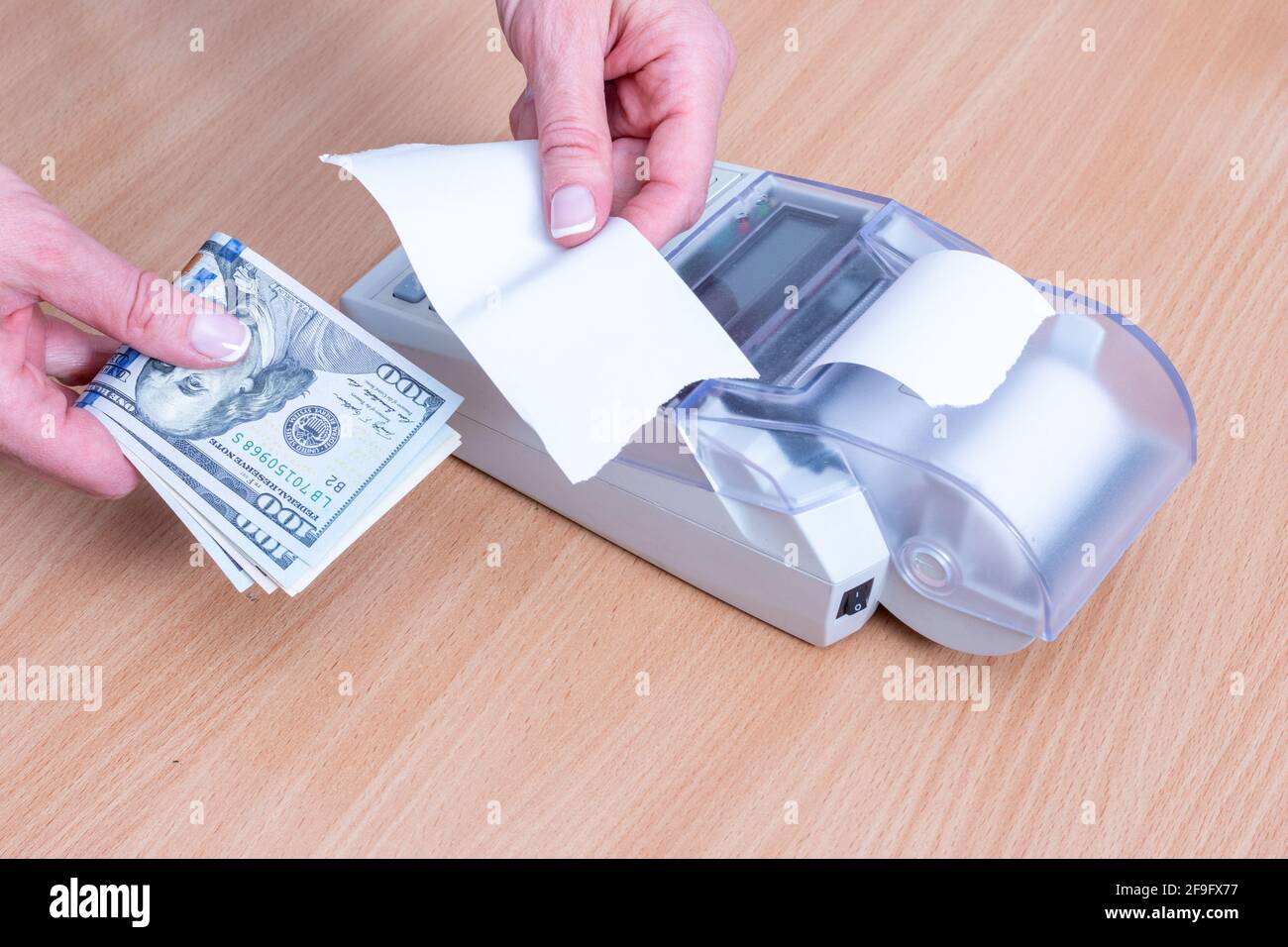 Business and financial concept. Close-up of a woman's hand holding several dollar bills above the cash register and holding a blank check form to pay Stock Photo