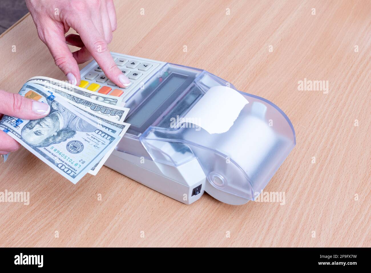 Business and financial concept. Close-up of a hand holding several hundred dollar bills and hand pressing the amount of purchases on a cash register o Stock Photo