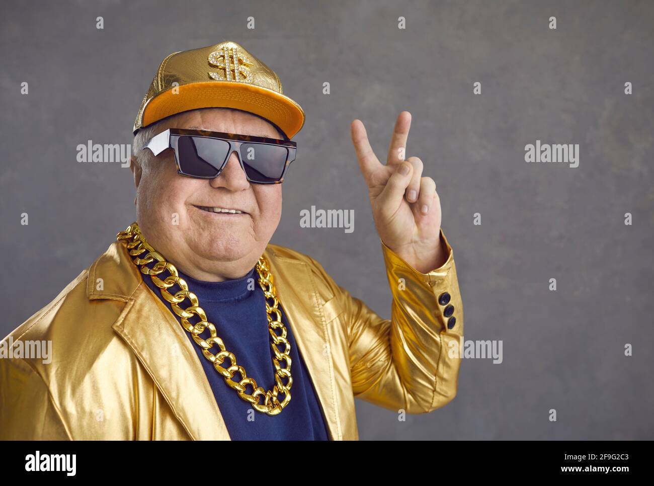 Funny and cheerful senior man in luxury clothes showing v-sign on gray background. Stock Photo