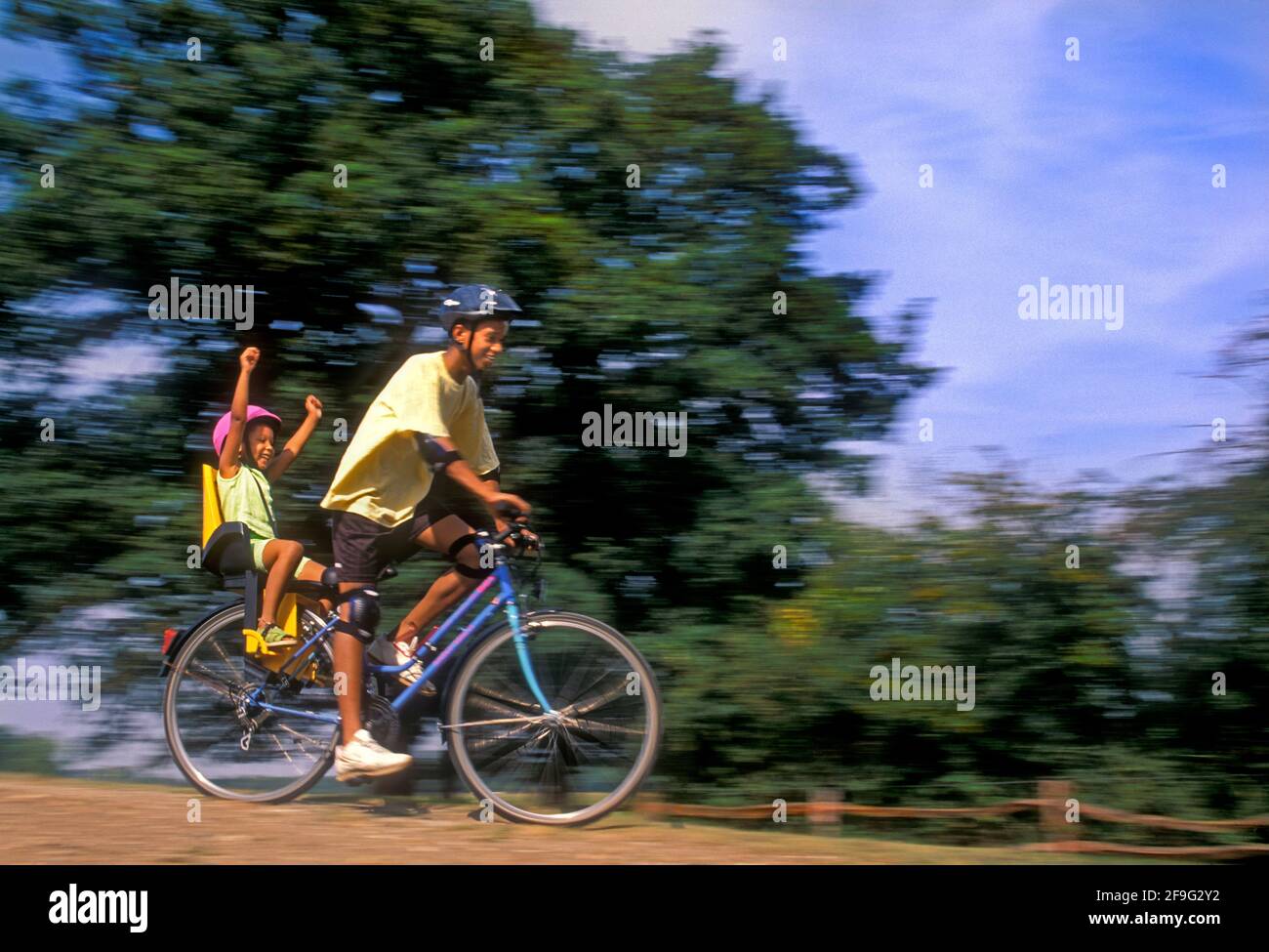 Staycation summer holiday fun UK Brother & Sister 14 years and 4 years British African Caribbean (Afro Caribbean) ethnicity, outside together enjoying a fun exhilarating safe off road summer bicycle ride Stock Photo
