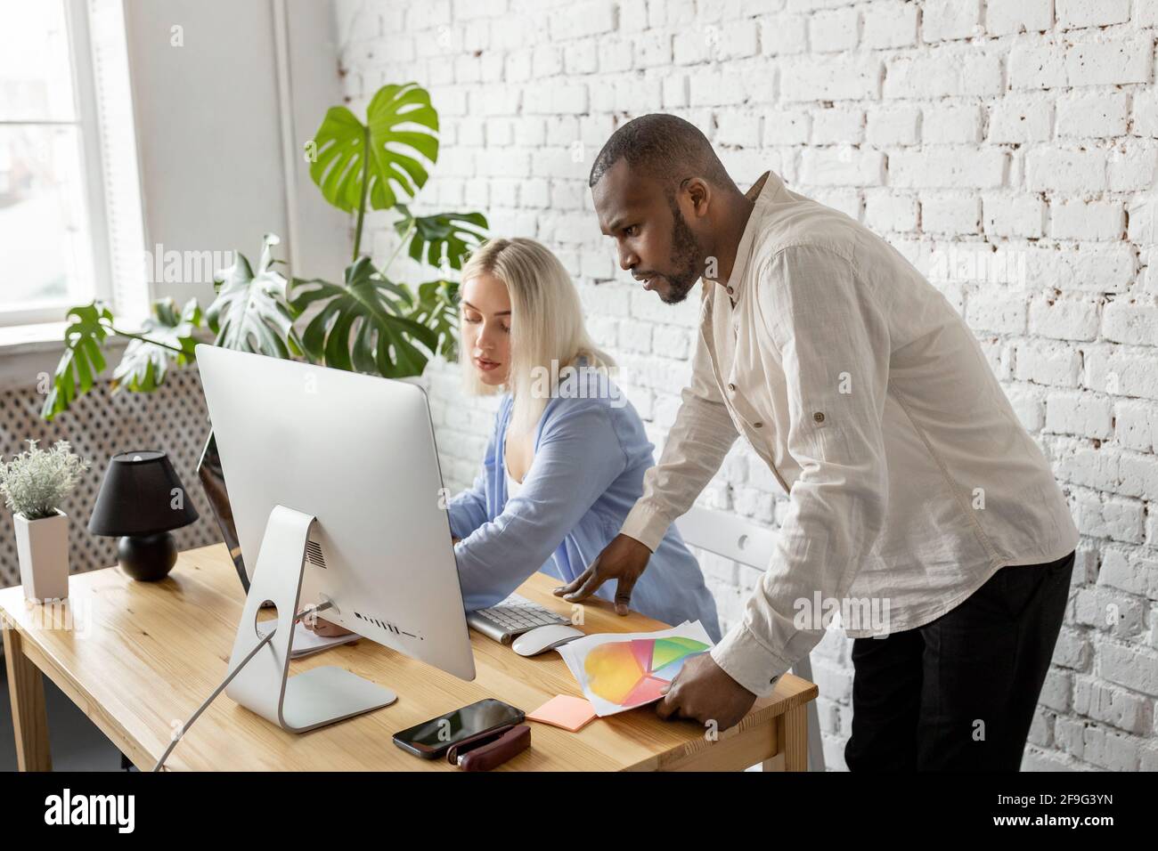Serious mixed race colleagues using computer, working on report, learning financial graphs. Focused business partners developing new project Stock Photo