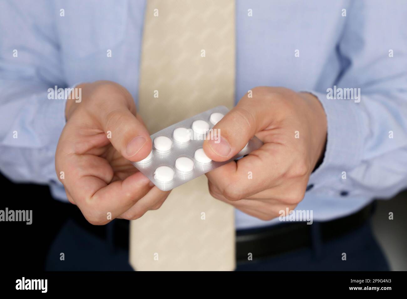 Man in office clothes taking pills, pack of medication in male hands close up. Concept of antidepressant, stress at work, vitamins, dose of drugs Stock Photo