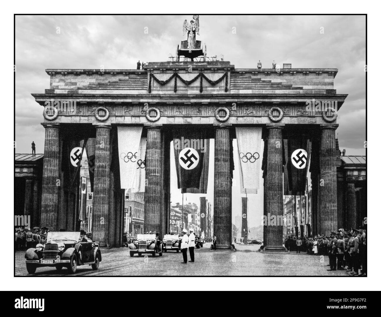 BERLIN OLYMPICS Vintage 1936 Brandenburg Gate Parade Berlin Nazi Germany with Nazi Swastika banners alongside official Olympic Games Flags Berlin Brandenburg Gate Nazi Germany   Parade with Adolf Hitler leading passes through the Brandenburg Gate on the way to the opening ceremonies of the Olympic Games. Berlin, Germany, August 1, 1936. Stock Photo