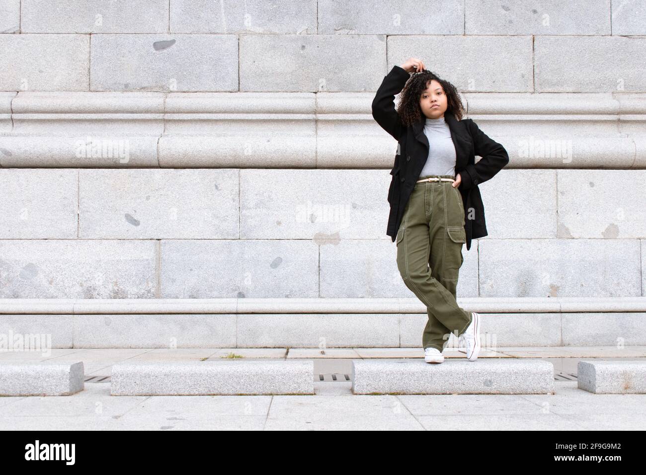 Black woman with curly hair standing in front of a stone brick wall ...