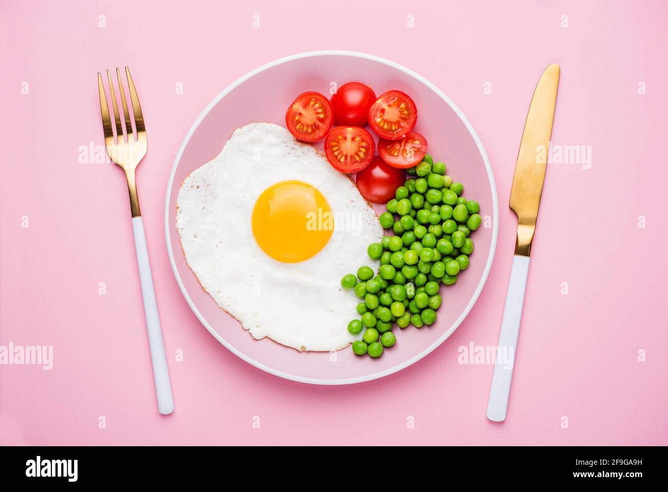 Fried egg with green peas and tomatoes on pink plate isolated on pink background. Healthy breakfast food Stock Photo