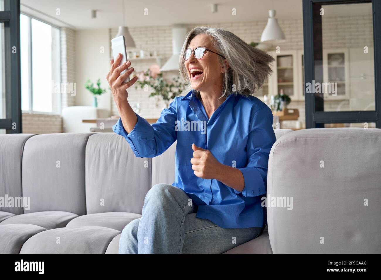 Surprised exited mature woman 60s aged at home with cellphone. Stock Photo