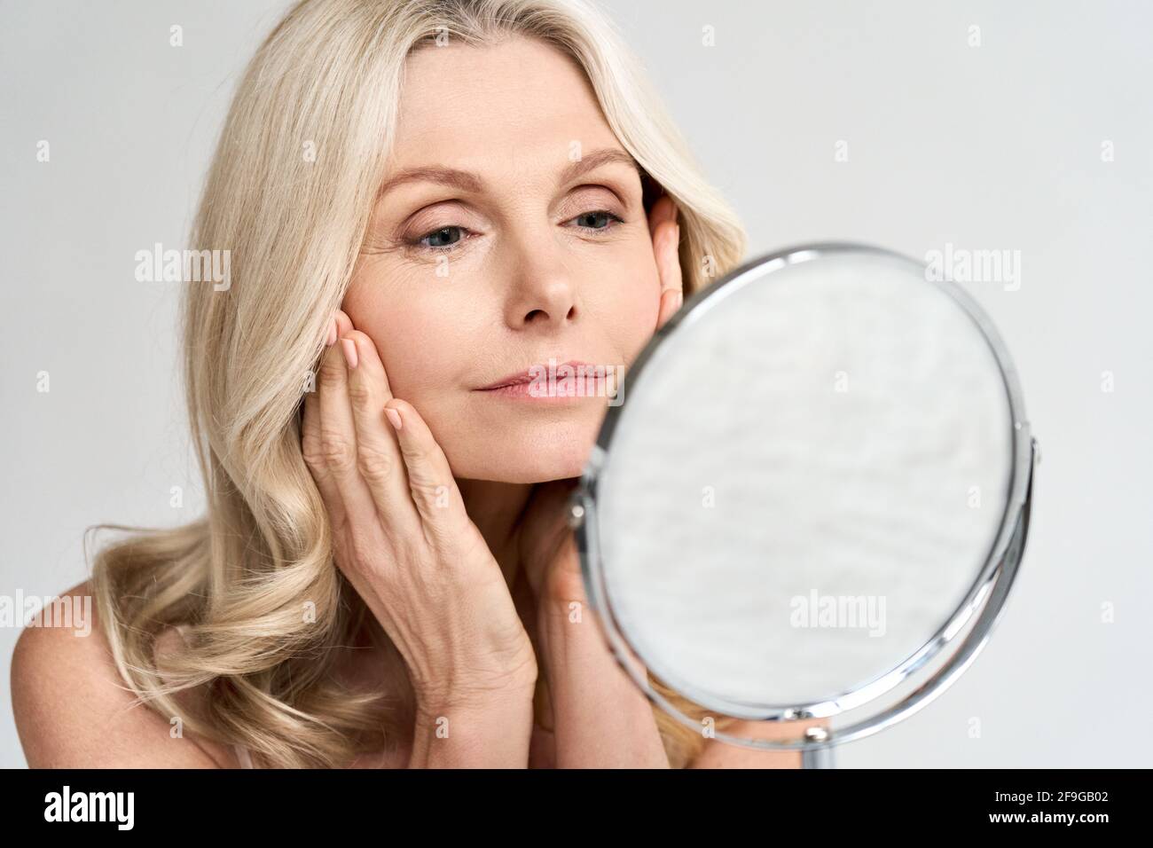 Closeup portrait middle age 50 woman looking at mirror, touching healthy skin. Stock Photo