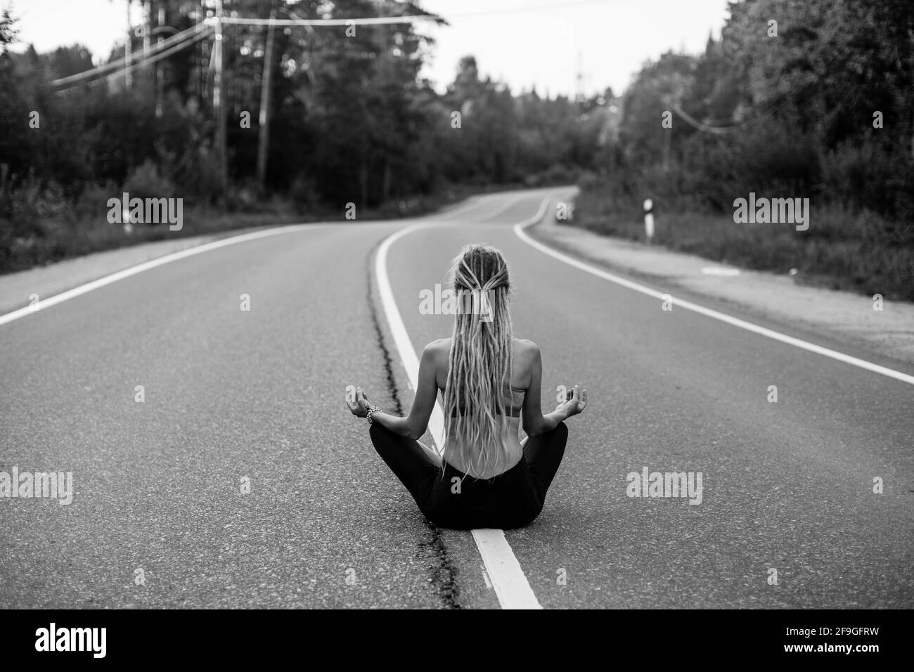 Yoga woman sitting in the middle of the road on Lotus position. Black ...