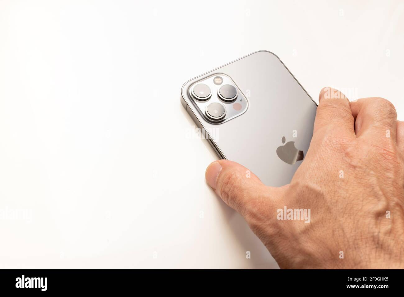 one hand holding the new Iphone 12 pro Max seen from the back, on a white background, copy space, horizontal Stock Photo