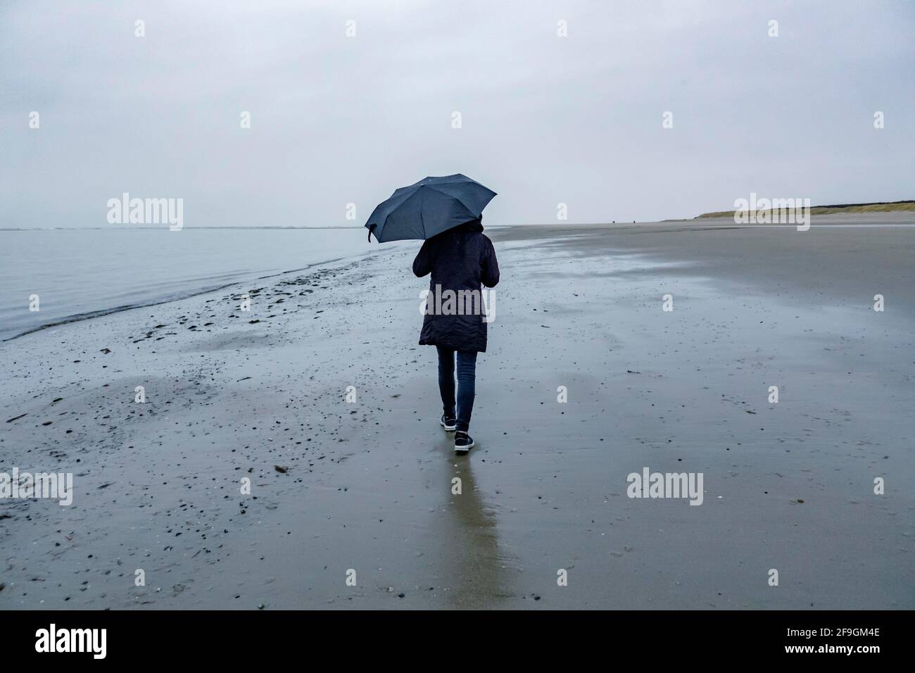 Woman with umbrella walking on the beach in rainy weather, Langeoog, East Frisian Islands, Lower Saxony, Germany Stock Photo