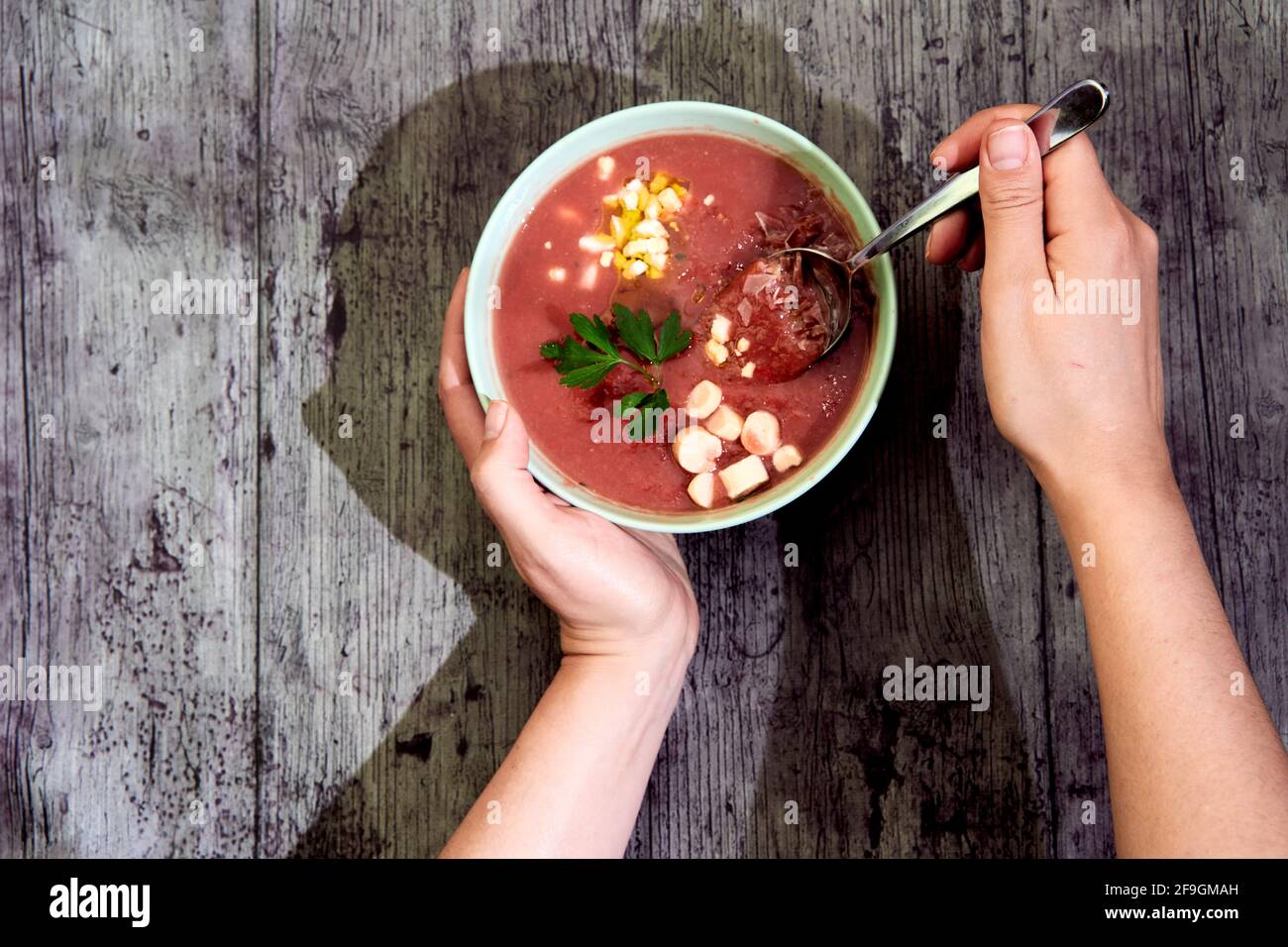 Zenith view of a gazpacho bowl with accompaniment garnish, being held by human hands, ready to taste with a spoon. With shadow. Concept of mediterrane Stock Photo