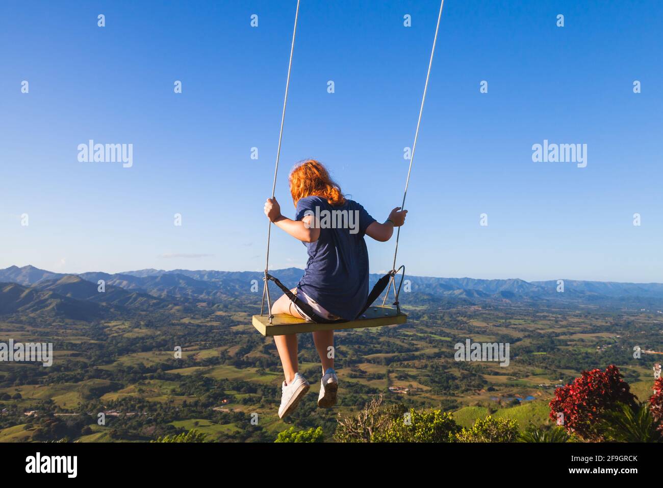 Red haired teenage girl swinging on a swing at Montana Redonda. Dominican Republic Stock Photo