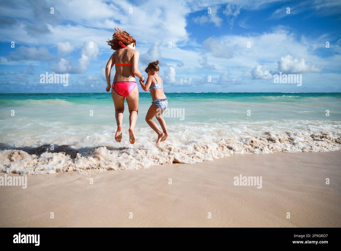 Girls jump in shore waves on a sunny day, Dominican Republic Stock Photo
