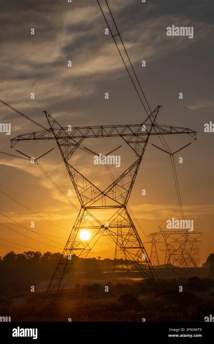 The sun rising behind a pair of towering electricity pylons Stock Photo