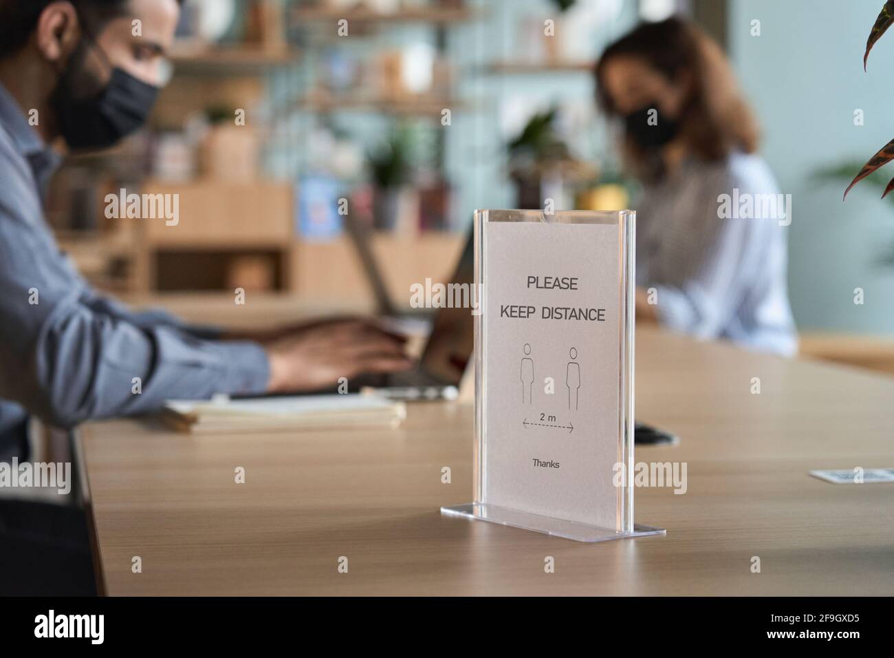Closeup of social distance sign standing on table with people working on pc. Stock Photo
