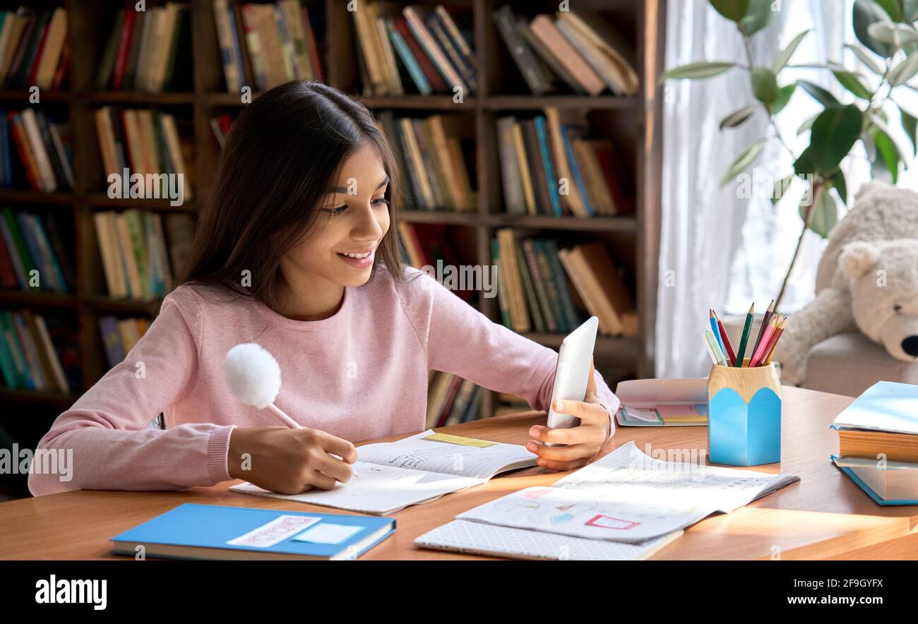 Happy smiling arab schoolgirl using phone for virtual online study at home. Stock Photo