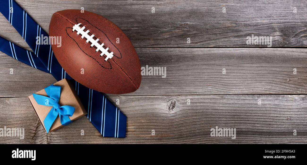 Fathers day concept with blue dress tie, American football and a gift box on rustic wooden background in flat lay format Stock Photo