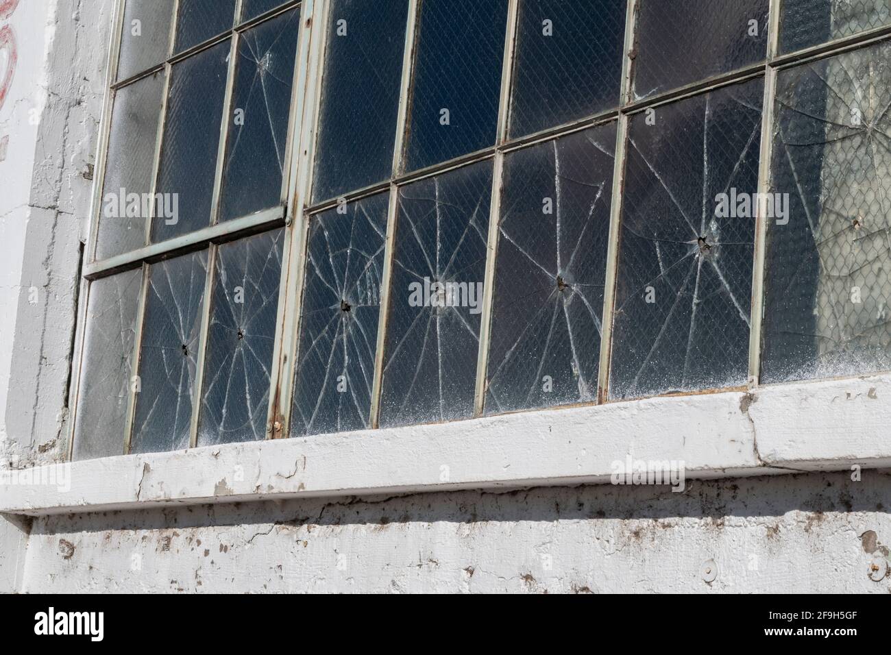 A row of windows in an abandoned building appears to have been shot with a pellet or bb gun. Stock Photo
