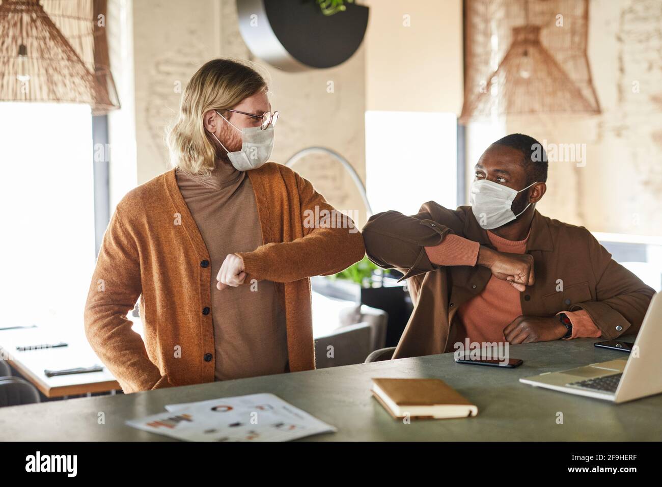 Portrait of two men wearing masks and bumping elbows during con tactless greeting in cafe or office, covid concept, copy space Stock Photo