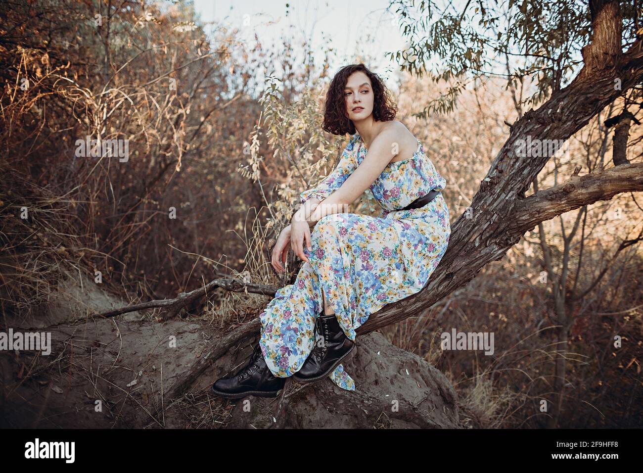 Young woman sits resting on leaning tree in autumn forest with her hands folded Stock Photo