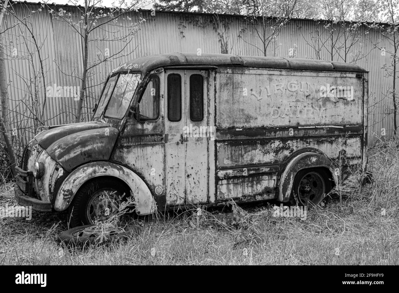 B&W photo of abandoned, rusted Virginia Dairies truck in front of metal building Stock Photo