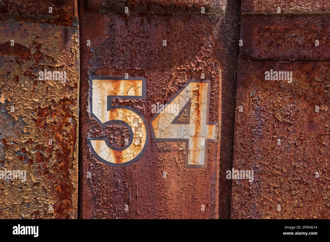 Number 54 painted on side of old rusted truck - number is white/cream colored, background is peeling paint on rusted metal Stock Photo