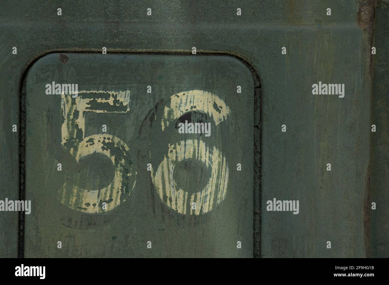 Number 56 painted on side of old rusted truck - number is white/cream colored, background is blue-green-grey Stock Photo