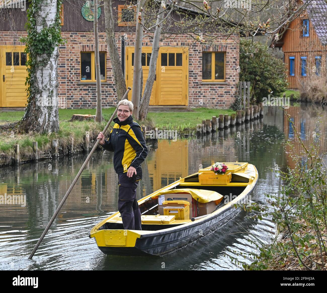 14 April 2021, Brandenburg, Lübbenau: Andrea Bunar, mail carrier, drives her yellow mail barge across a river (waterway in the Spreewald) at the start of the mail delivery season. Mail carrier Andrea Bunar is bringing a bit of normalcy to the Spreewald during the Corona pandemic: since Wednesday, she has been delivering letters and parcels to residents again with her barge. Some things have fortunately remained the same, such as the unspoiled nature in the Spreewald, said Bunar at the start on the water. The 50-year-old delivers to 65 households; she steers her barge on the eight-kilometer tou Stock Photo