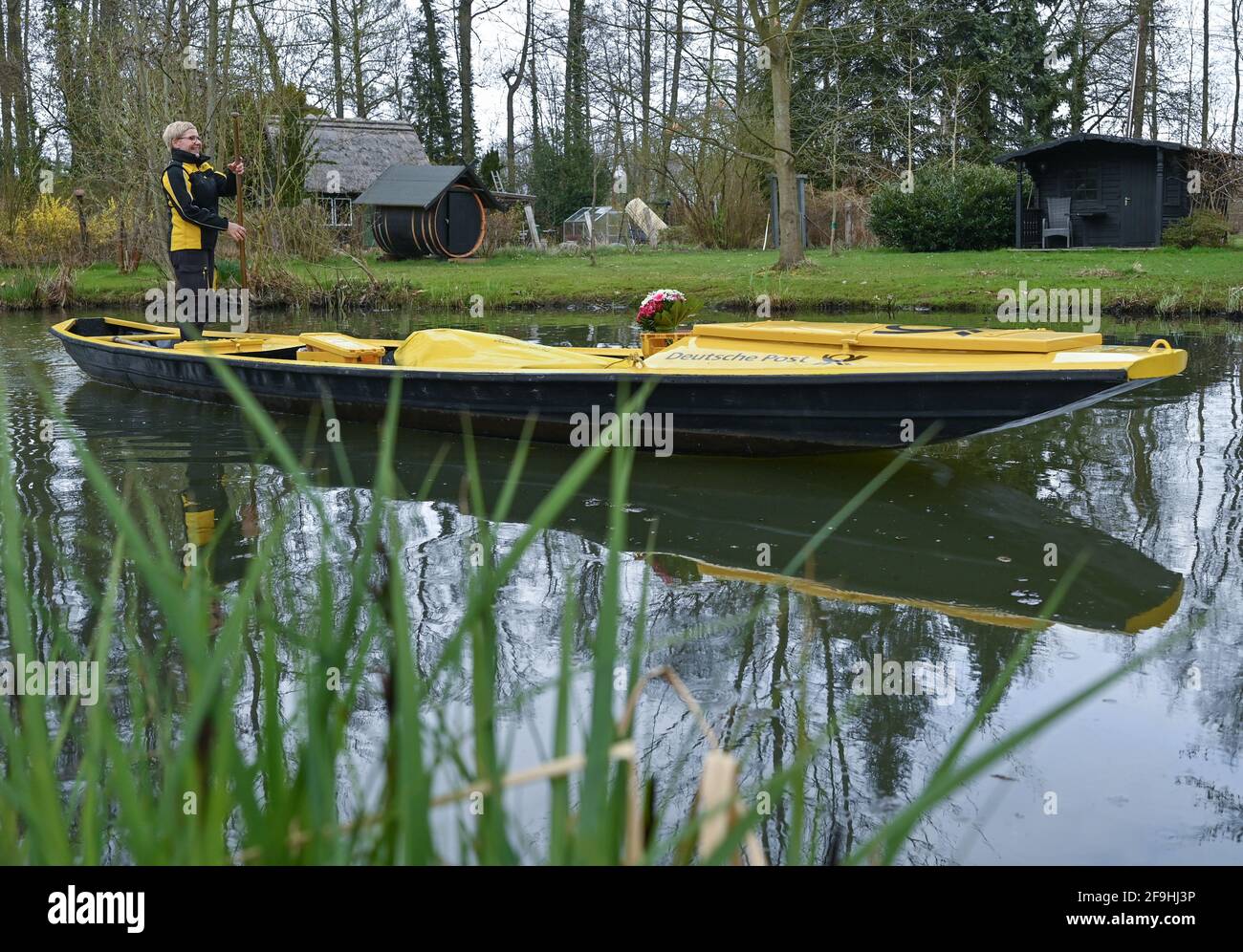 14 April 2021, Brandenburg, Lübbenau: Andrea Bunar, mail carrier, drives her yellow mail barge across a river (waterway in the Spreewald) at the start of the mail delivery season. Mail carrier Andrea Bunar is bringing a bit of normalcy to the Spreewald during the Corona pandemic: since Wednesday, she has been delivering letters and parcels to residents again with her barge. Some things have fortunately remained the same, such as the unspoiled nature in the Spreewald, said Bunar at the start on the water. The 50-year-old delivers to 65 households; she steers her barge on the eight-kilometer tou Stock Photo