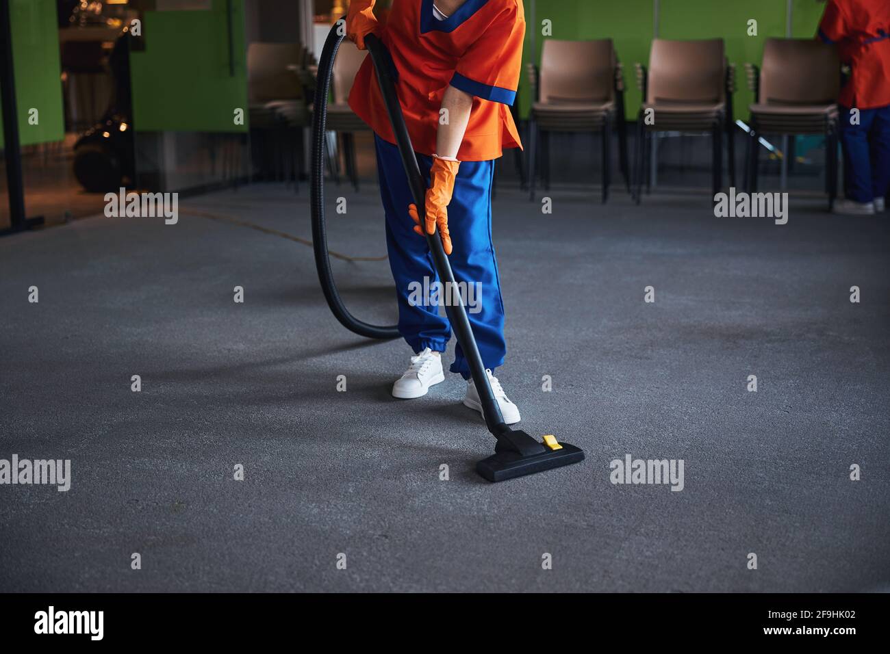Female janitor vacuuming the carpeted floor in the conference hall Stock Photo