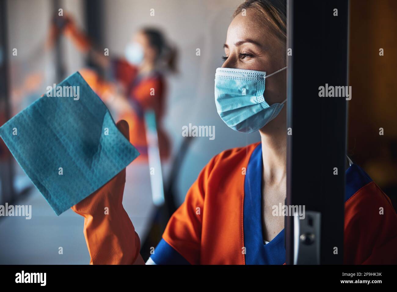 Pensive janitor in a disposable face mask doing the cleaning Stock Photo