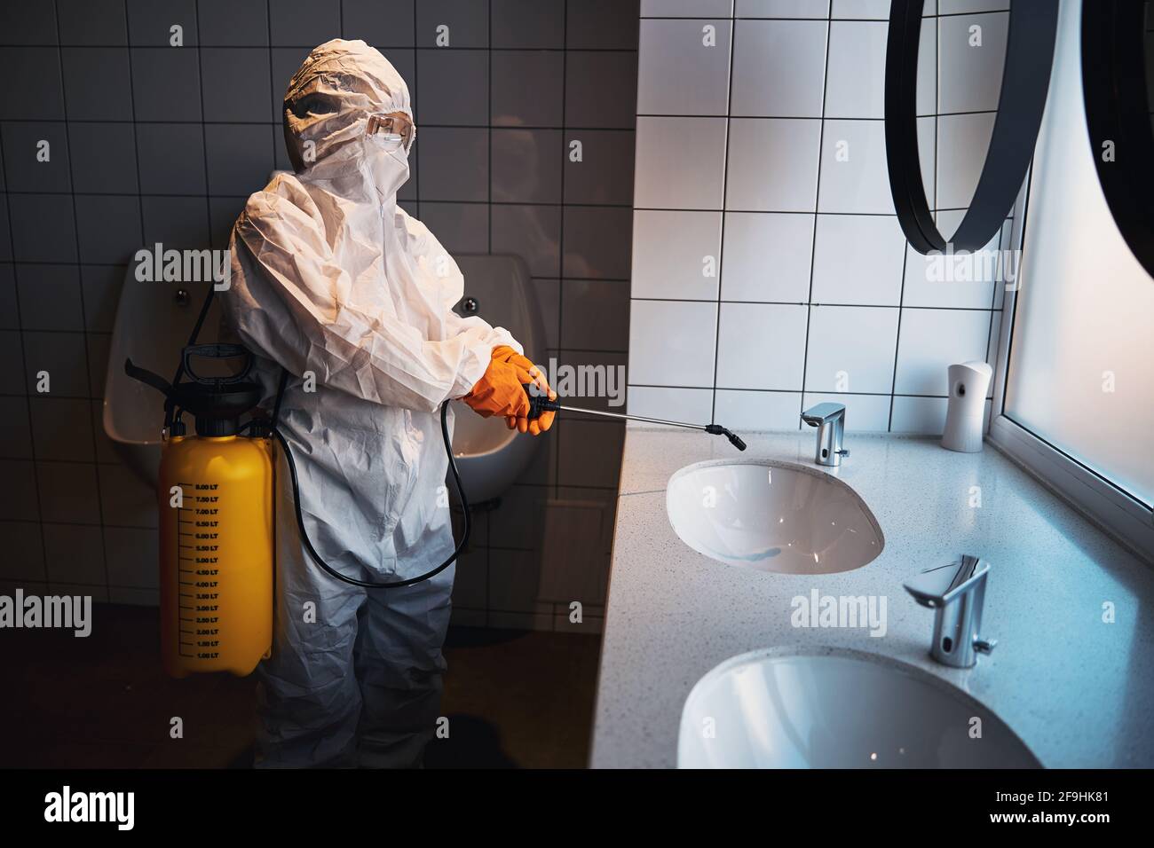 Professional female cleaner in a hazmat suit disinfecting surfaces