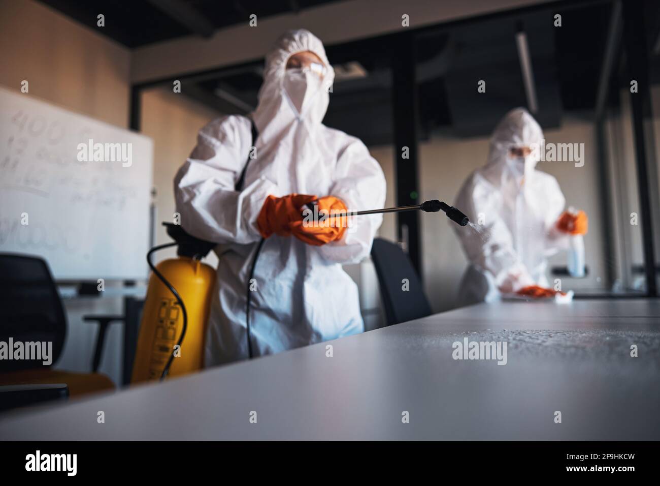 Trained janitorial staff sanitizing the surfaces of desks Stock Photo