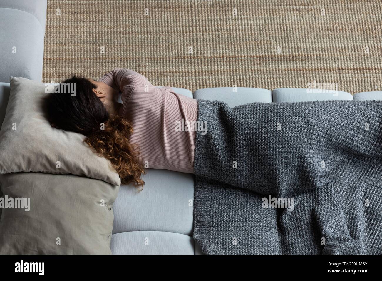 Exhausted latin woman sleep on couch in clothes under plaid Stock Photo