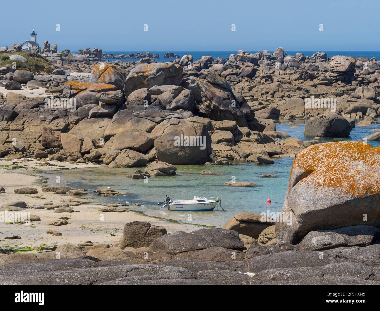 A small fishing boat at anchor in a cove on the rocky coast of northern Finistère in Brittany. In the distance the semaphore of Brignogan-Plage* Stock Photo