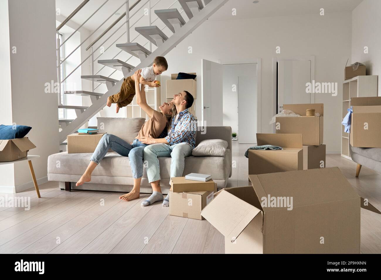 Happy young family playing with kid son together in new home on moving day. Stock Photo
