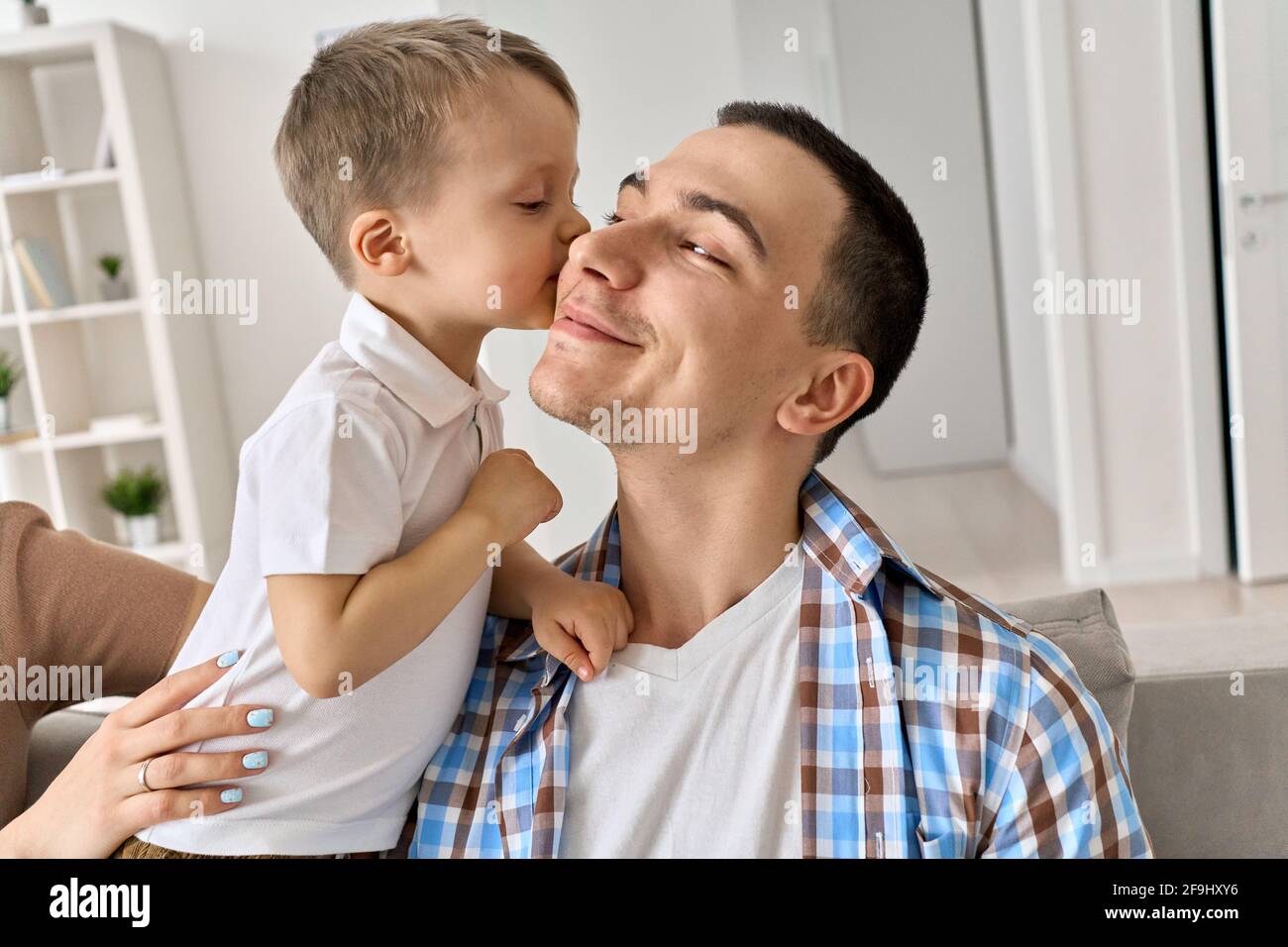 Cute toddler kid son kissing smiling dad on cheek at home. Stock Photo