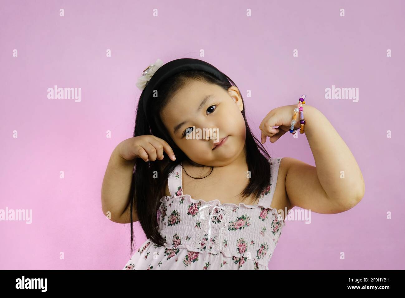 A cute young chubby Asian girl is posing, showing off her biceps to show how strong she is. Bright pink background. Stock Photo