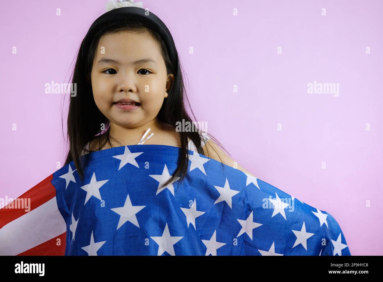 A cute young chubby Asian American girl is fiddling around with a large American flag to hang in front of her home for the 4th of July Independence da Stock Photo