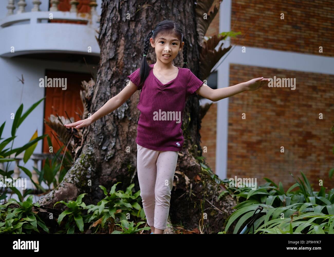 A cute young Asian girl is walking and balancing herself on the root of