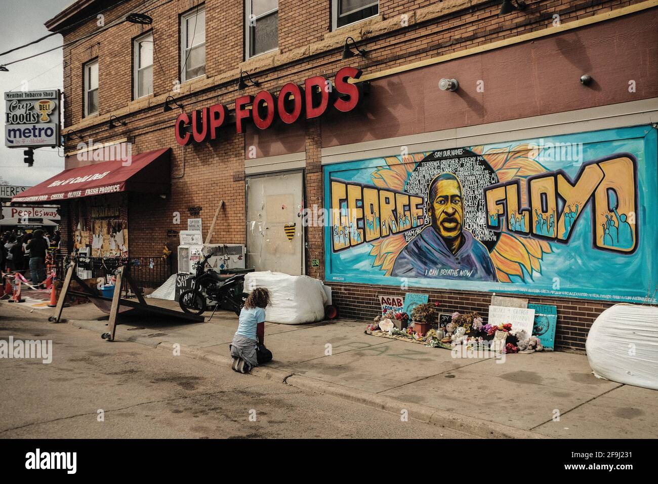 Minneapolis, United States. 18th Apr, 2021. A woman pays respect to a mural of George Floyd by the Cup Foods where he was killed by Minneapolis Police Officer Derek Chauvin in Minneapolis, Minnesota. On the night before closing statements are set to be delivered in the trial of former Minneapolis Police Officer Derek Chauvin over the killing of George Floyd, a crowd congregated at George Floyd Plaza where relatives of black men killed by police delivered speeches and made statements. Credit: SOPA Images Limited/Alamy Live News Stock Photo