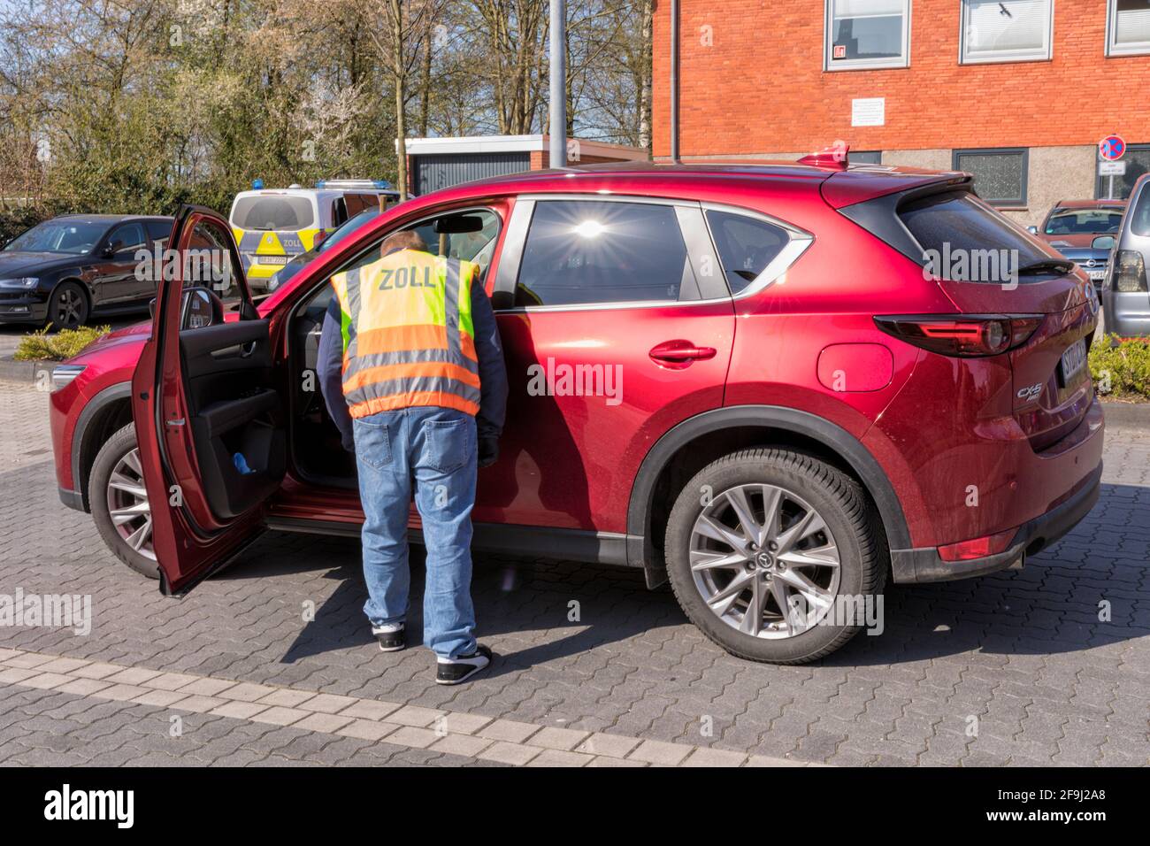 A German customs official in plainclothes, wearing a warning vest, examining a car. Stock Photo