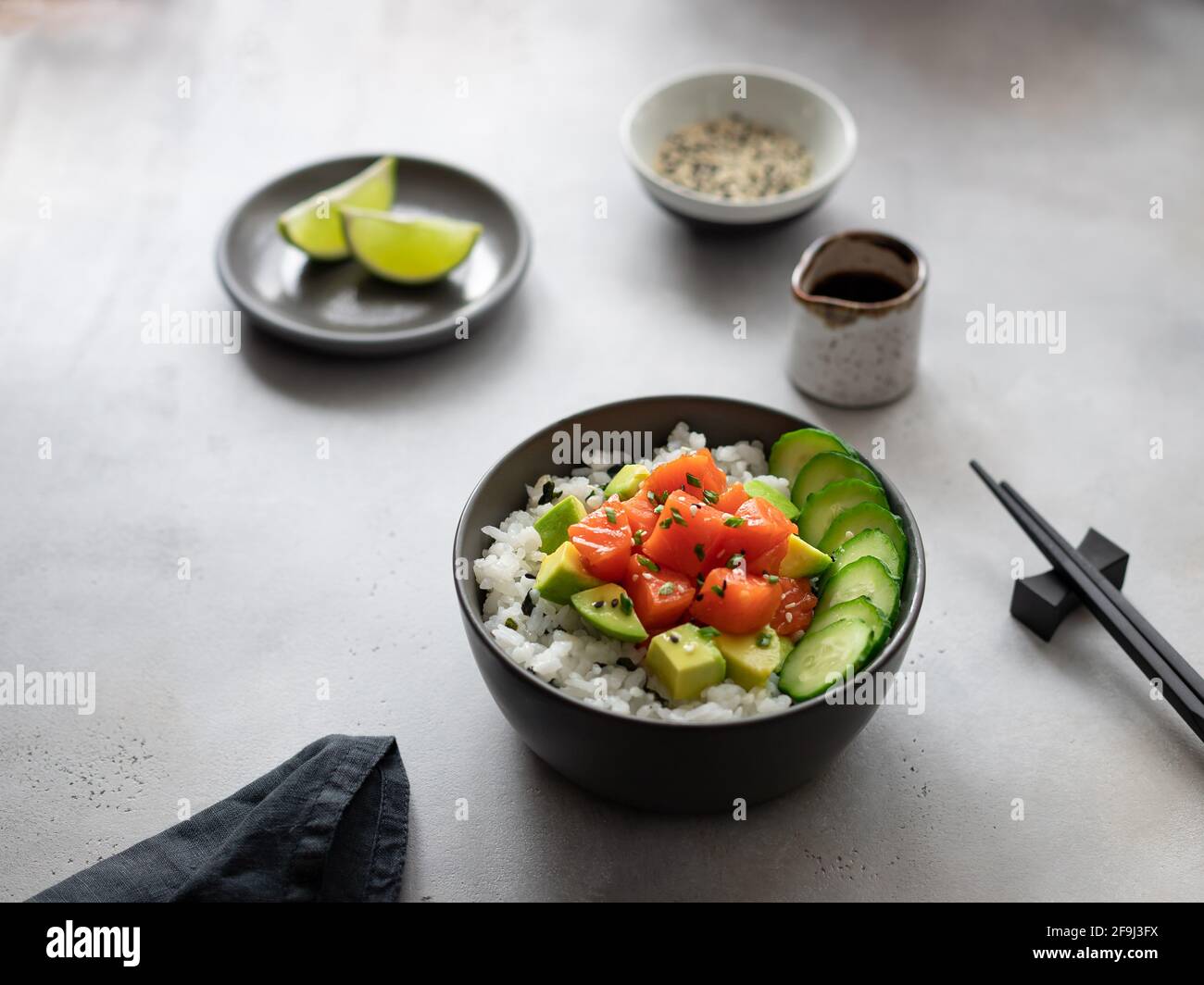 salmon fish poke bowl with avocado, cucumber, rice, sesame seeds and soy sauce on gray background. traditional asian food. side view, horizontal image Stock Photo