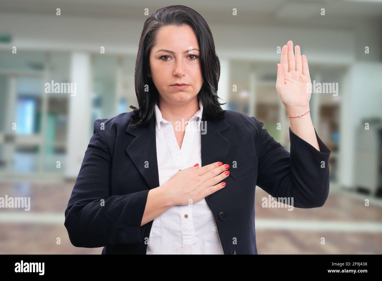 Serious female entrepreneur businesswoman making honest oath gesture showing palm touching chest heart with office room background Stock Photo