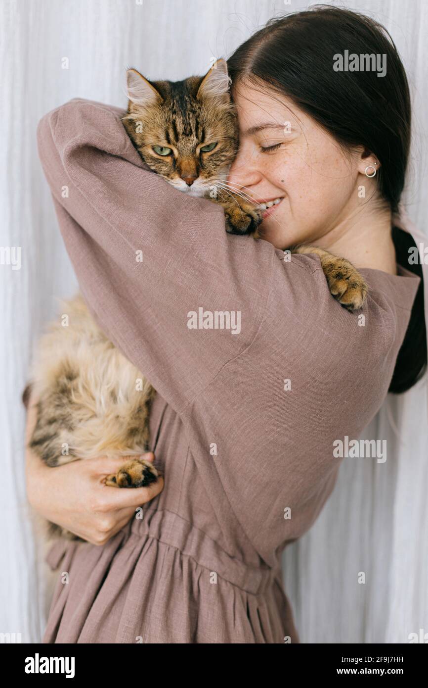 Stylish happy woman in linen dress hugging cute cat on background of ...