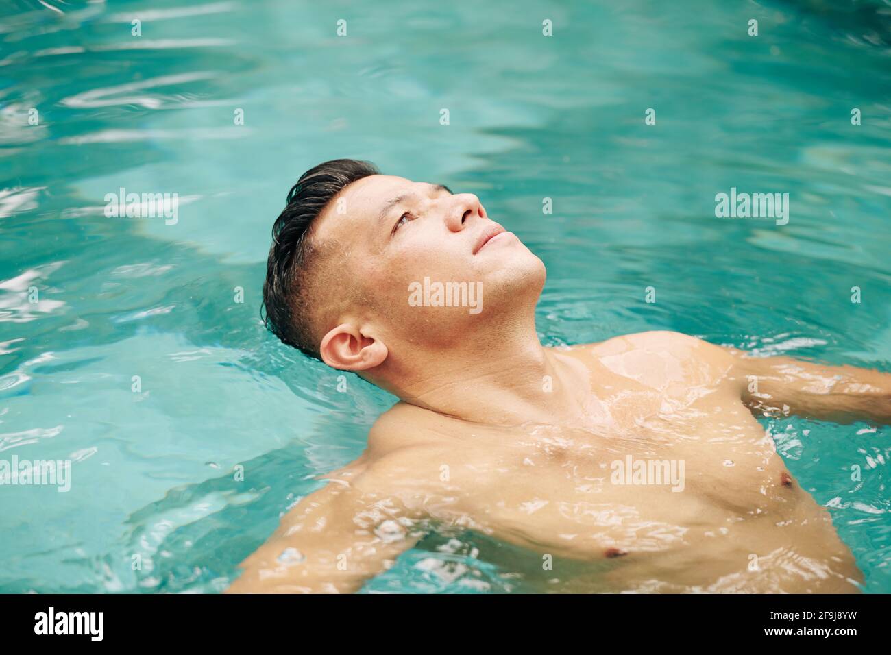 Fit man floating on back in swimming pool and looking at sky Stock Photo